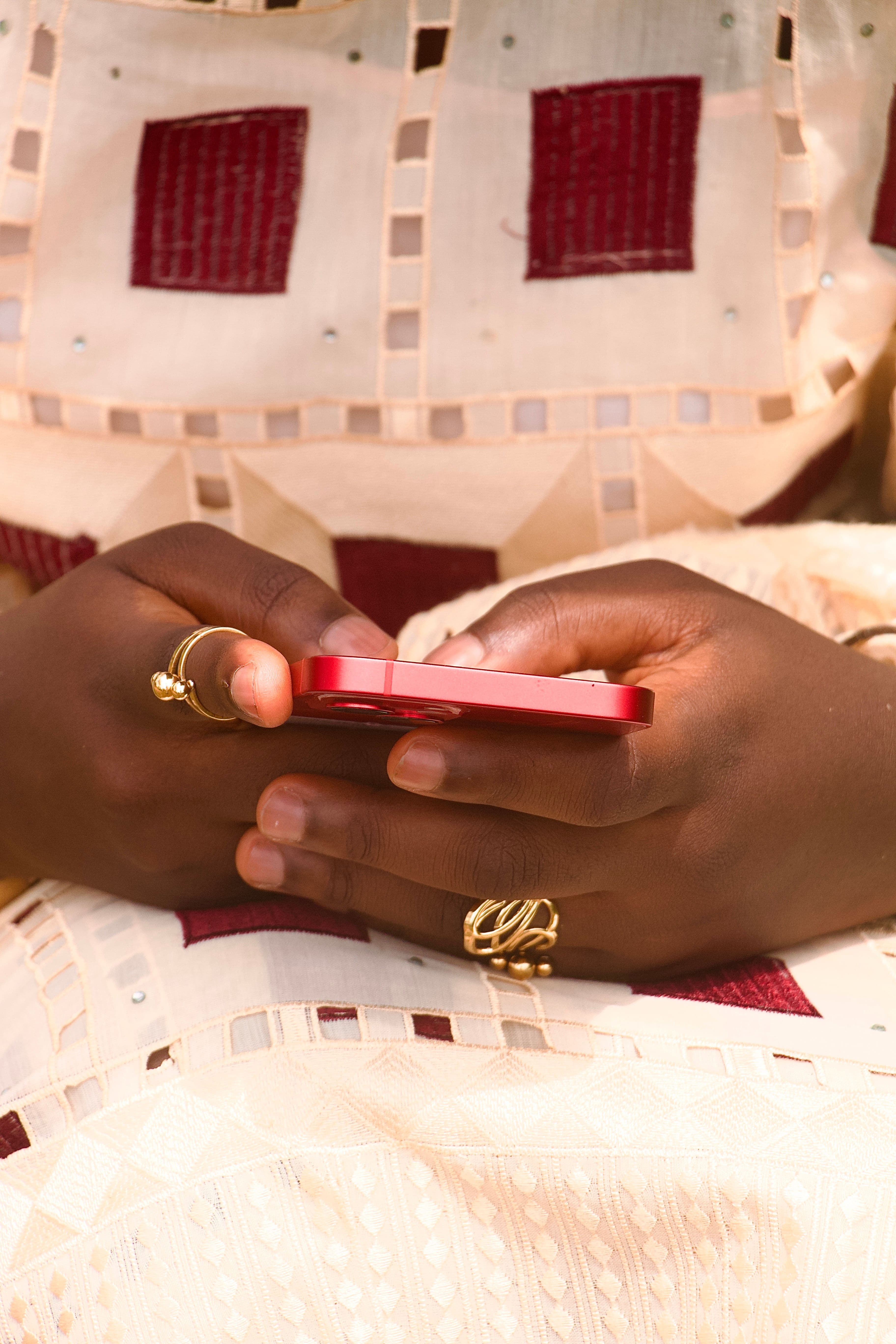 Mains tenant un smartphone KoLa — textile traditionnel et bagues dorées, modernité africaine