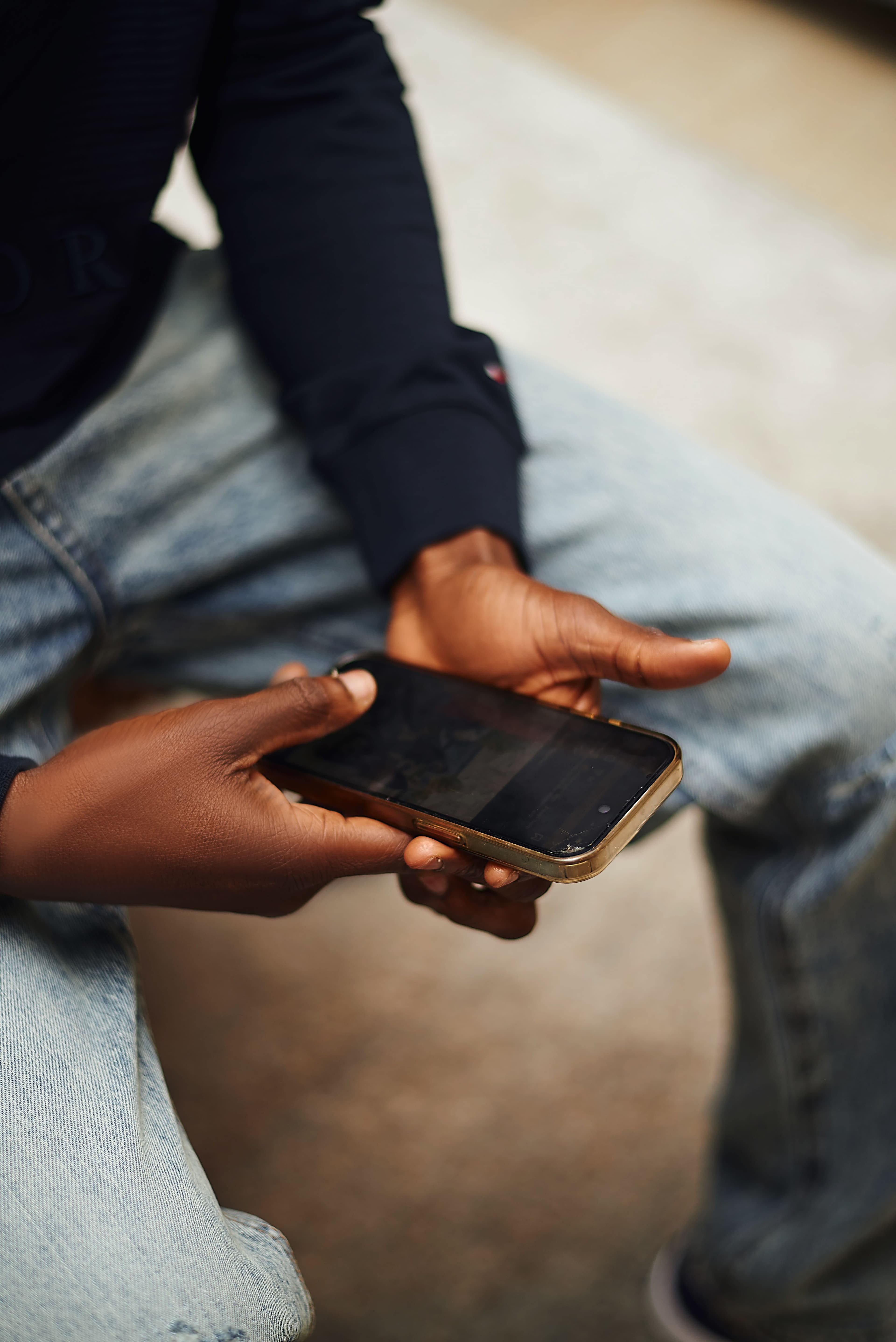 Mains tenant un smartphone — denim premium, usage quotidien KoLa